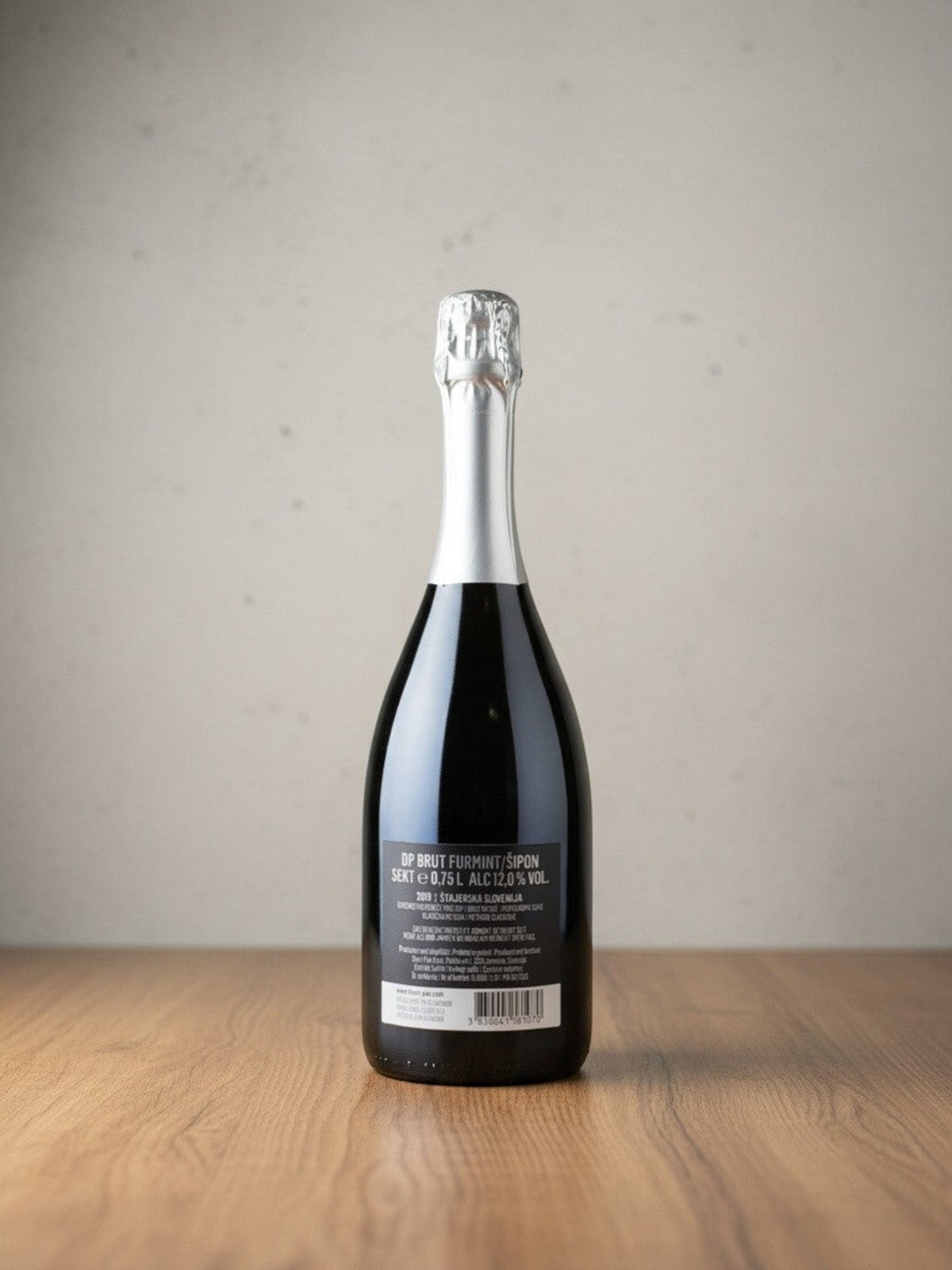 Rückseite einer Goldener Zwilling Dveri-Pax Furmint Brut 2019 Sektflasche mit Etikett auf einem Holztisch
